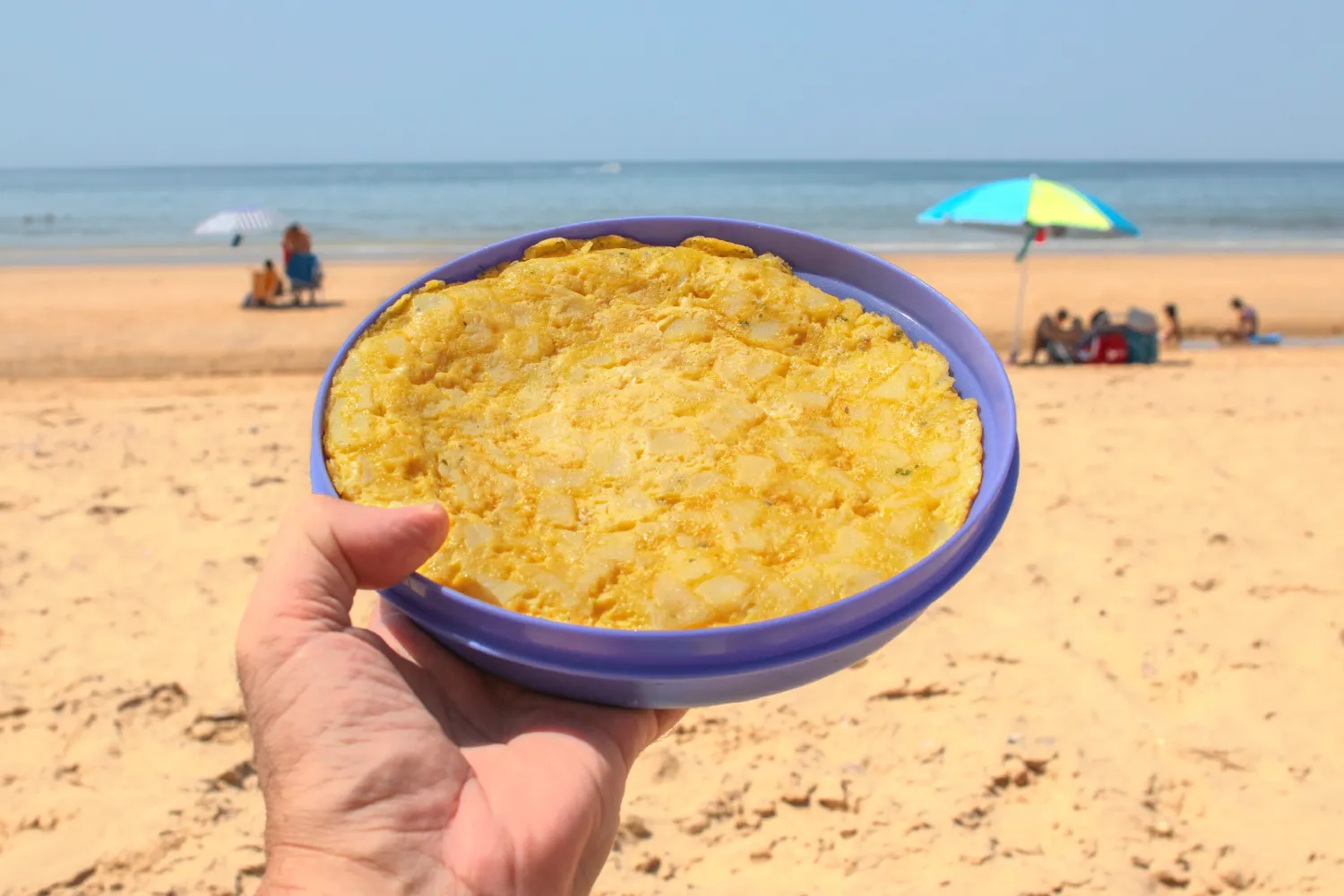 hand-holding-potato-omelette-tupperware-beach-background